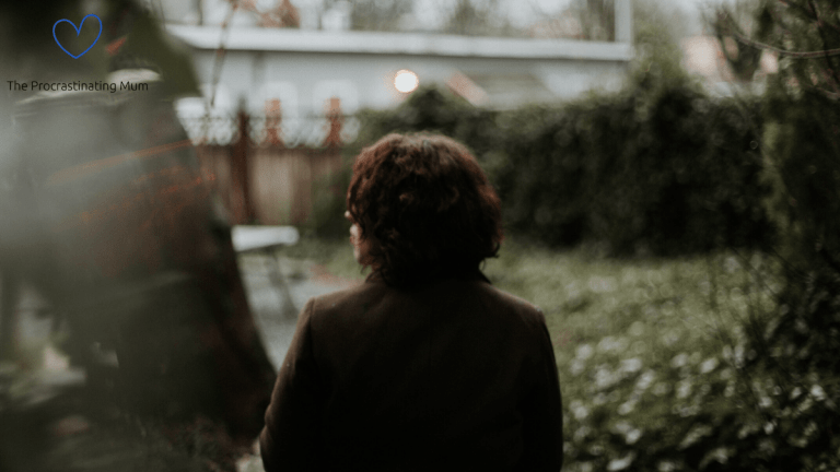 A woman is walking away from the camera. She has dark hair and wearing a dark jacket. She is walking outside and everything looks a little dark