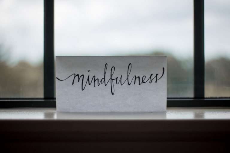 In front of a window is a single piece of paper. The paper is stood up and has mindfulness written on it