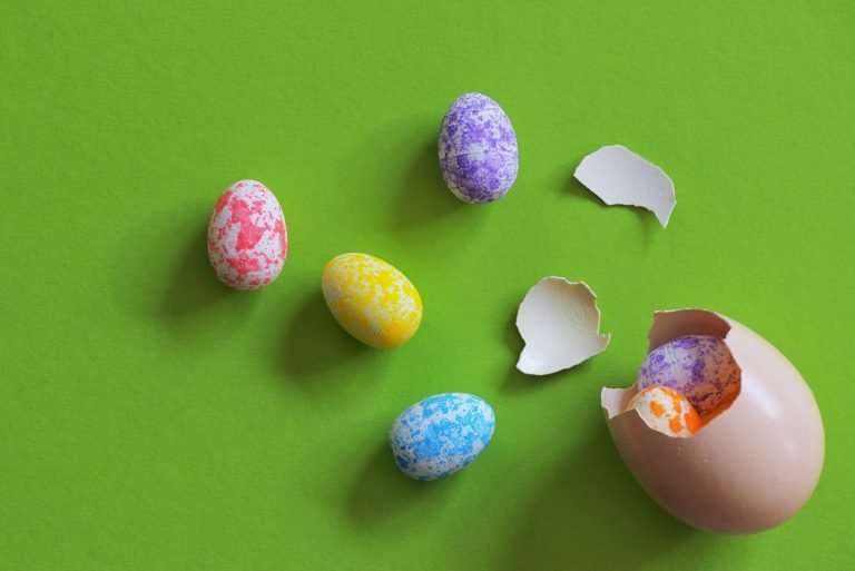 A green background with an egg cracked open with coloured eggs spilling out