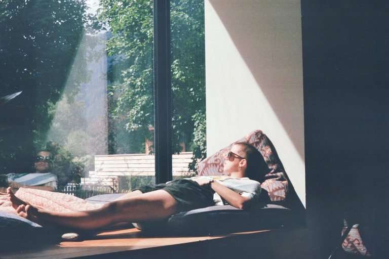 A person in shorts, t-shirt and sunglasses laying down on cushions looking out of a massive window