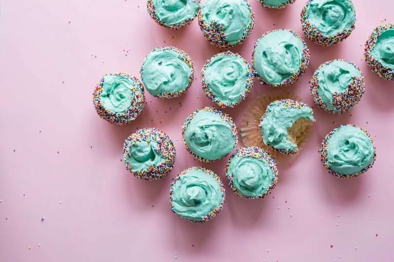 A pink background. There are lots of cupcakes with mint coloured icing and multicoloured sprinkles