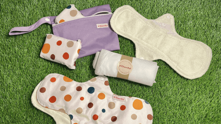 Cherriful reusable pads are resting on grass. Some are face-up, and some are face down, showing their spots. The carry case is on the grass with a folded up pad poking out. The wash bag is folded up in the middle of the picture