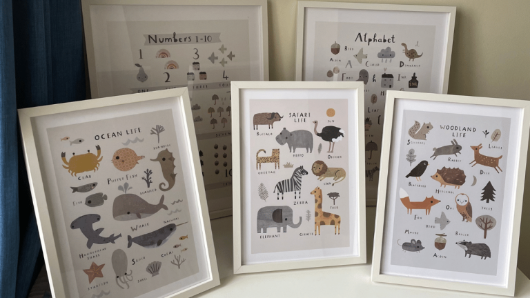 On a white unit, there are 5 frames. two large and 3 smaller. Within the smaller frames are three different prints with animals drawn on them and their names underneath. There is Ocean Life, Safari Life and Woodland Life. The larger frames which are slightly behind are numbers 1 - 10 with different objects and the alphabet with different pictures for each letter