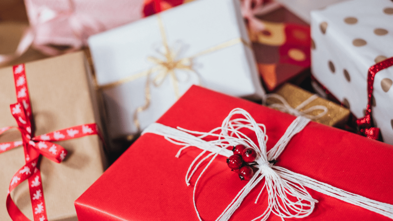 Lots of packages are wrapped up in Christmas wrapping paper. Some boxes are in focus, and some are not. The wrapping papers are red, white, gold, spotty and lots of ribbons