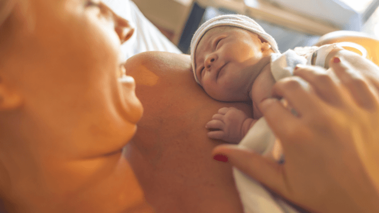 A woman has just given birth. She is holding her newborn baby, smiling